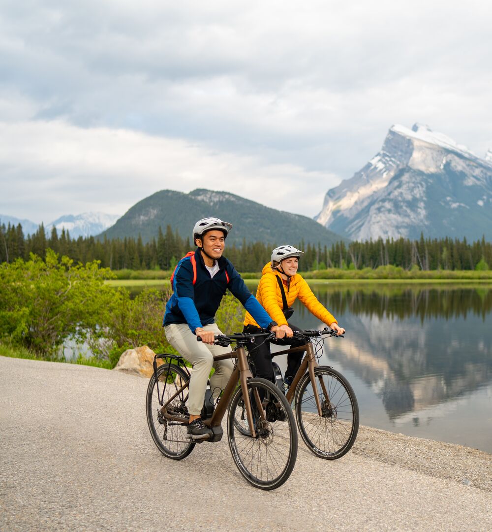 Two road cyclists ride past Vermilion Lakes with Mount Rundle in the background in Banff National Park.