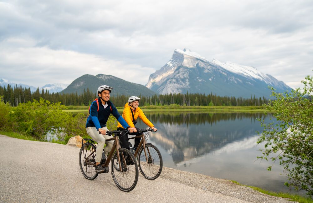 Two road cyclists ride past Vermilion Lakes with Mount Rundle in the background in Banff National Park.