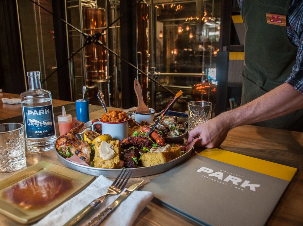 A server places a full, family-style platter down on a table at PARK Distillery on Banff Avenue, the perfect place for a family-style dining experience in Banff National Park.