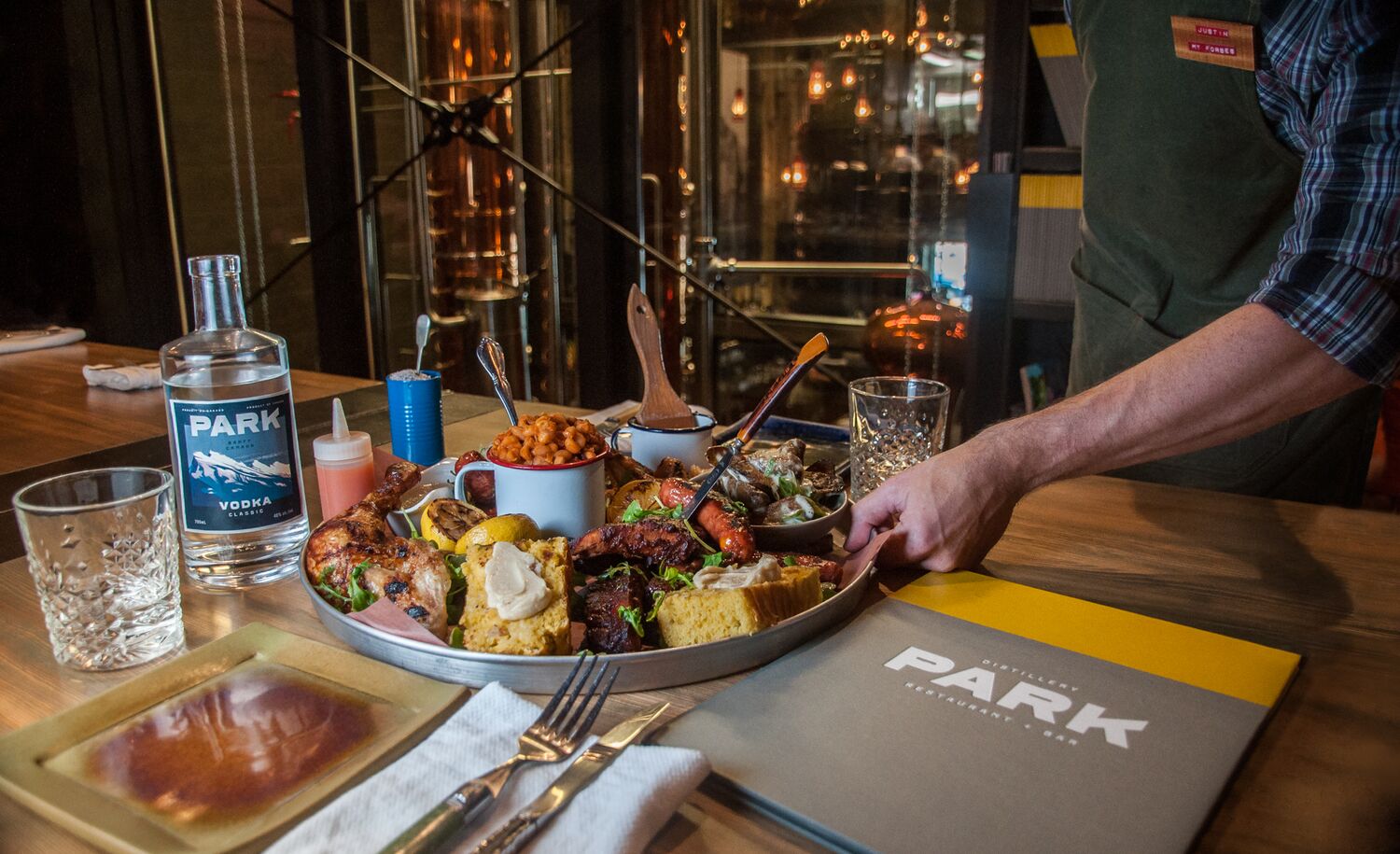 A server places a full, family-style platter down on a table at PARK Distillery on Banff Avenue, the perfect place for a family-style dining experience in Banff National Park.