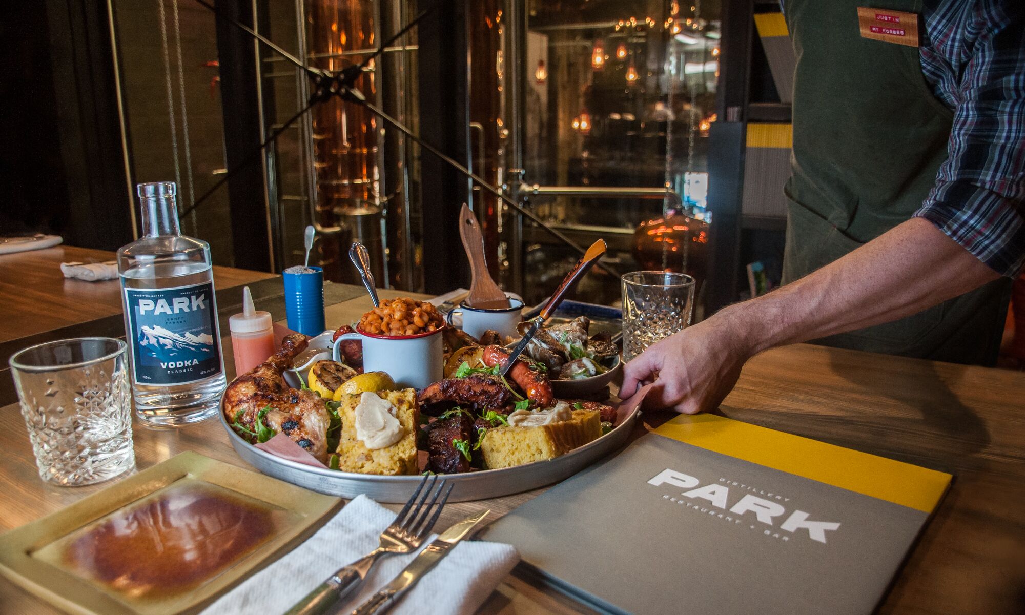 A server places a full, family-style platter down on a table at PARK Distillery on Banff Avenue, the perfect place for a family-style dining experience in Banff National Park.
