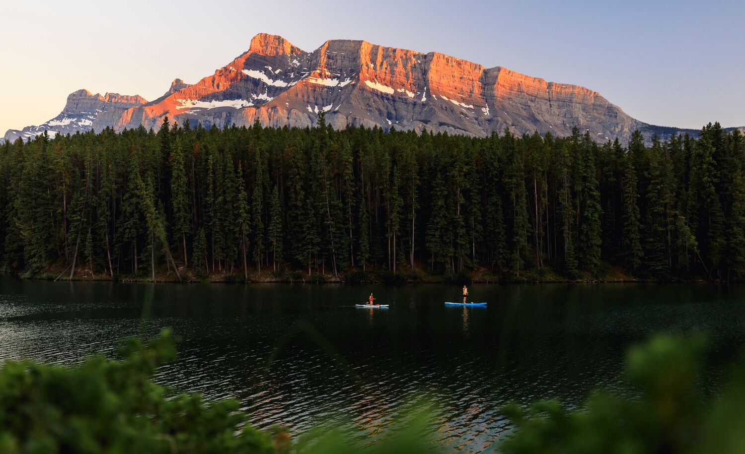 Two standup paddleboarders on Johnson Lake at sunset in Banff National Park.