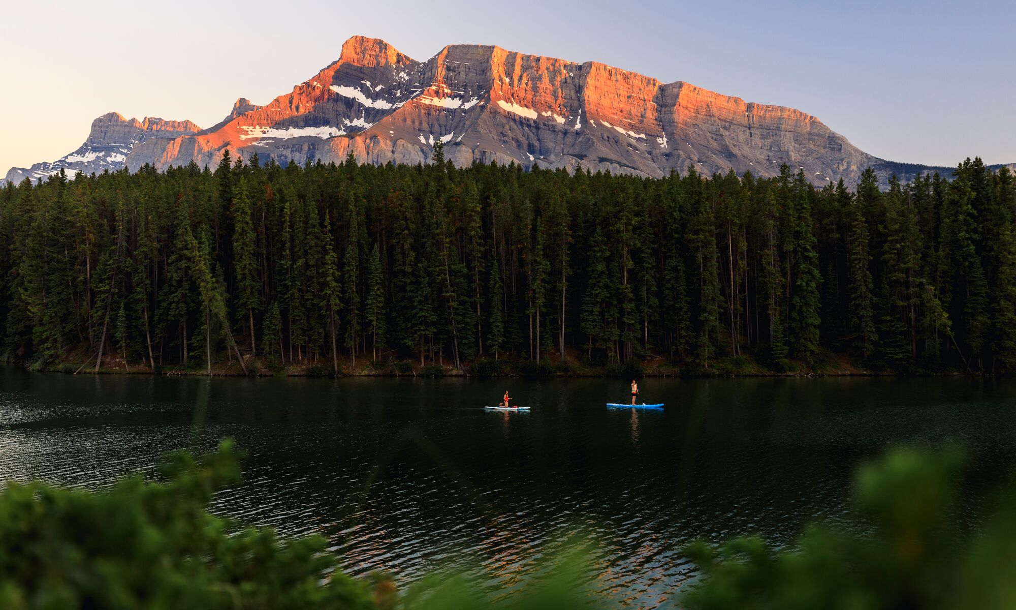 Two standup paddleboarders on Johnson Lake at sunset in Banff National Park.