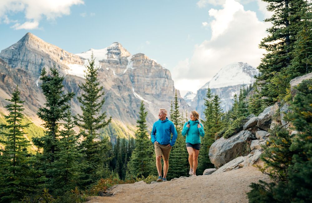 Two people hiking in Banff National Park on a trail at Lake Louise in the summer with mountains behind them.