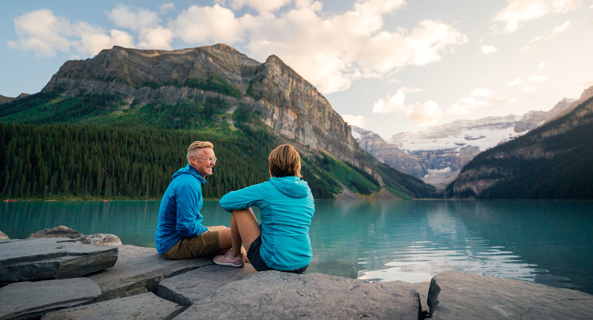 Two people sitting on the lakeshore at Lake Louise in the summer