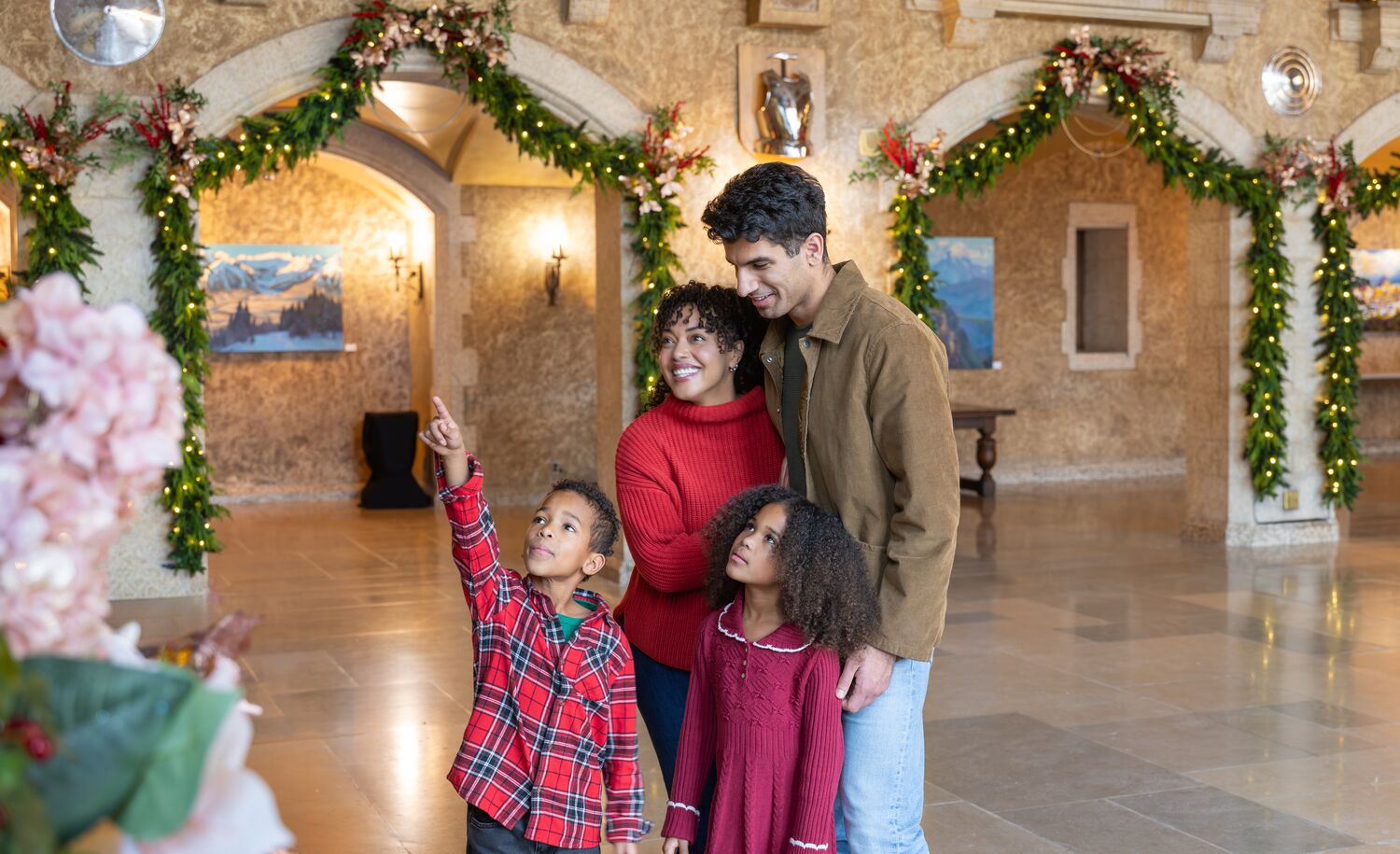 Family and couple standing beneath festive Christmas lights inside the Fairmont Banff Springs during the holiday season in Banff National Park, enjoying one of the must-see Christmas events in the Canadian Rocky Mountains