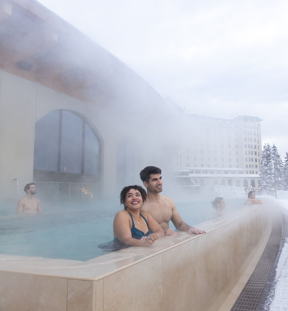 A couple in an outdoor hot pool at a spa in Lake Louise