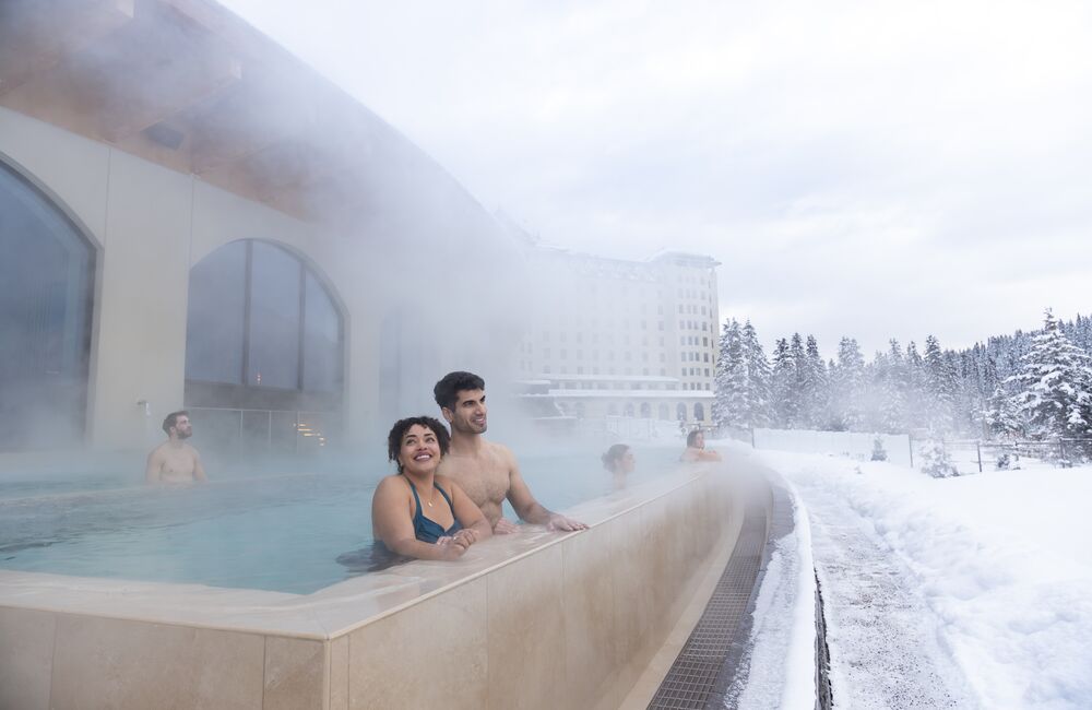A couple in an outdoor hot pool at a spa in Lake Louise