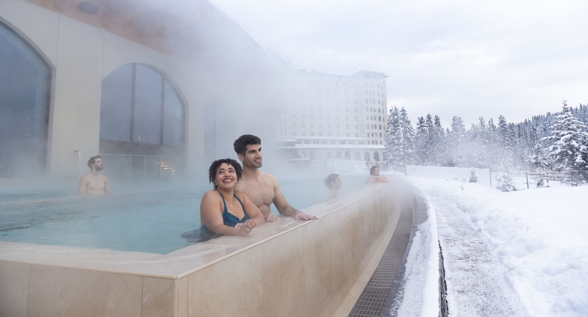 A couple in an outdoor hot pool at a spa in Lake Louise
