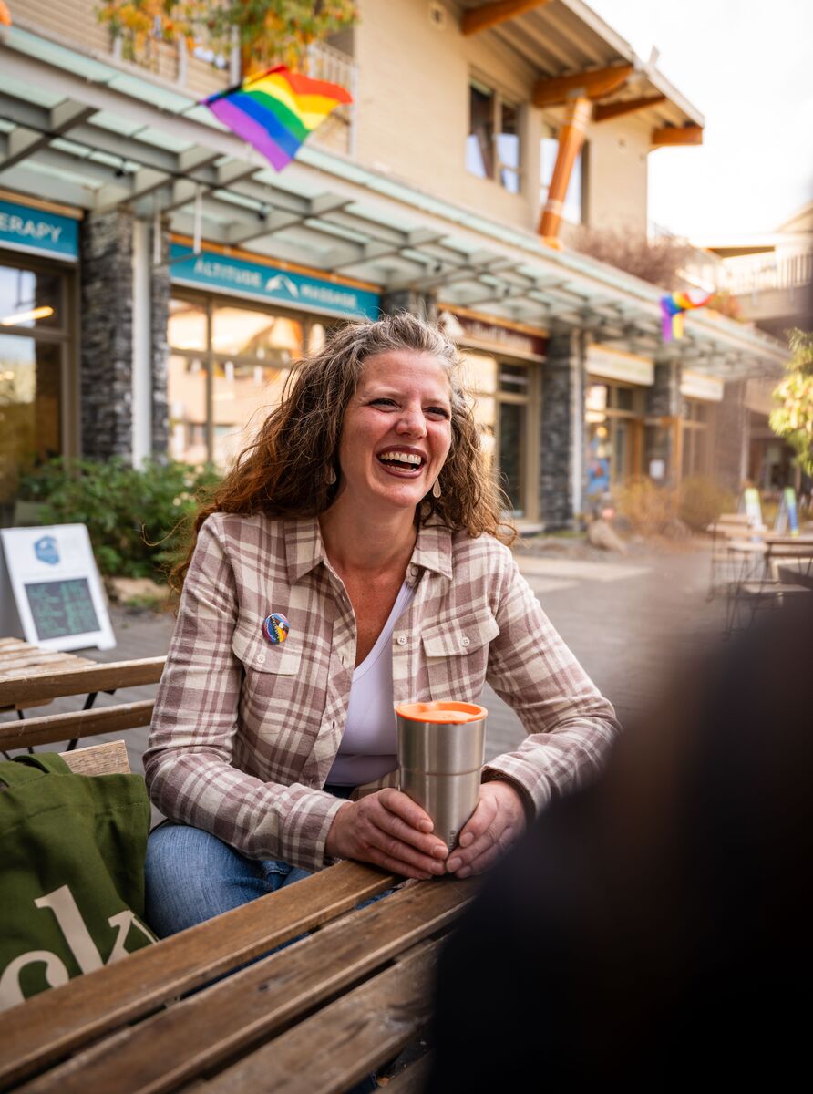 A woman sits at a table outside having a conversation with a friend in Banff National Park.