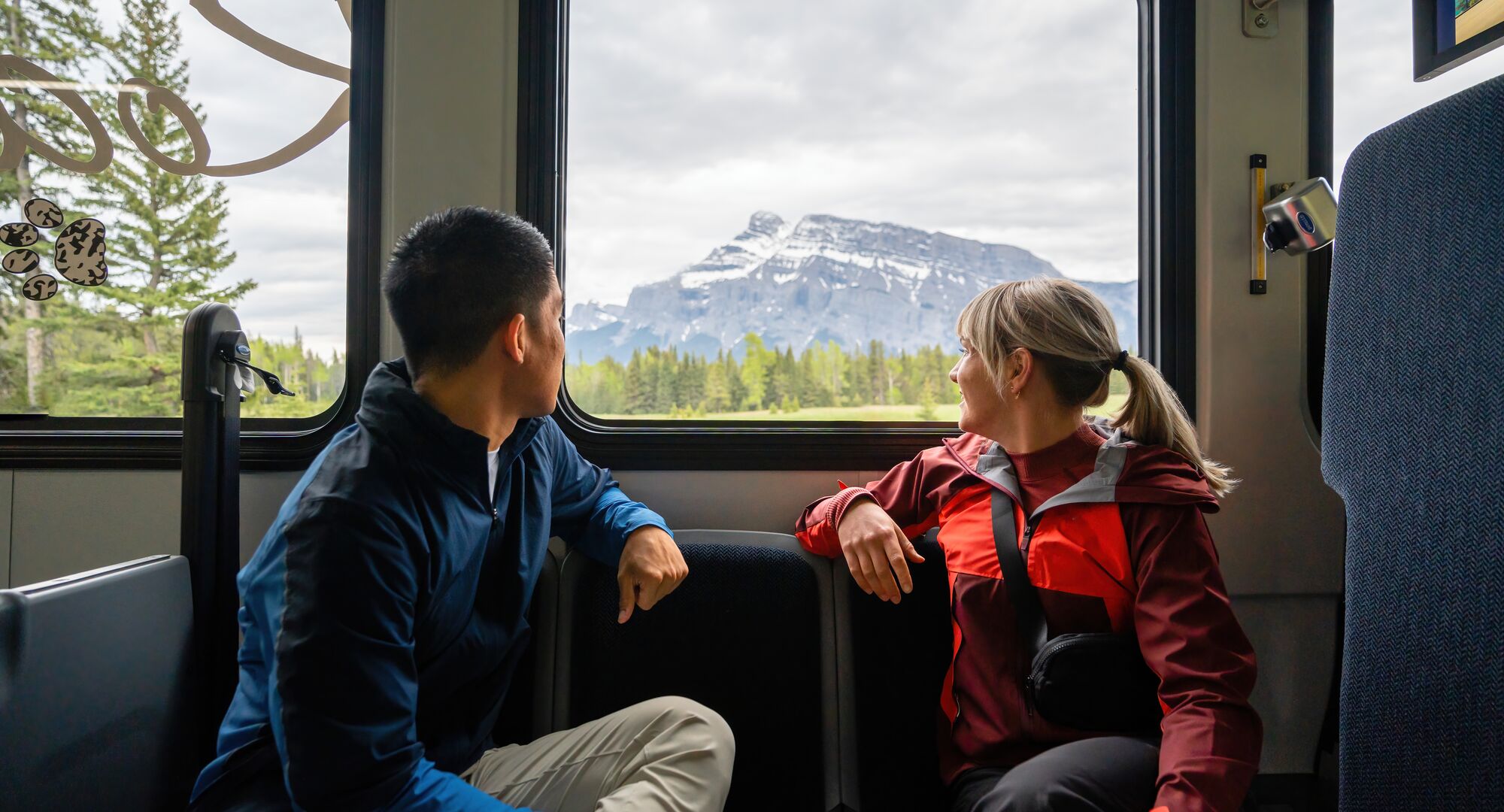 Two people riding the bus, looking out the window to mountain views in Banff National Park.