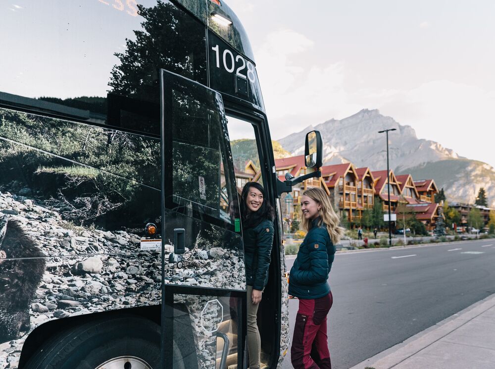 Two people get on a Roam Transit bus in the summer, heading to hike in Lake Louise.