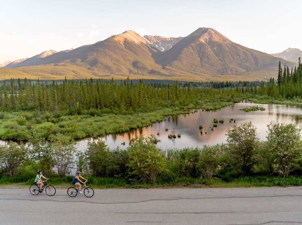 Two people bike along Vermilion Lakes Road at sunset in Banff National Park.