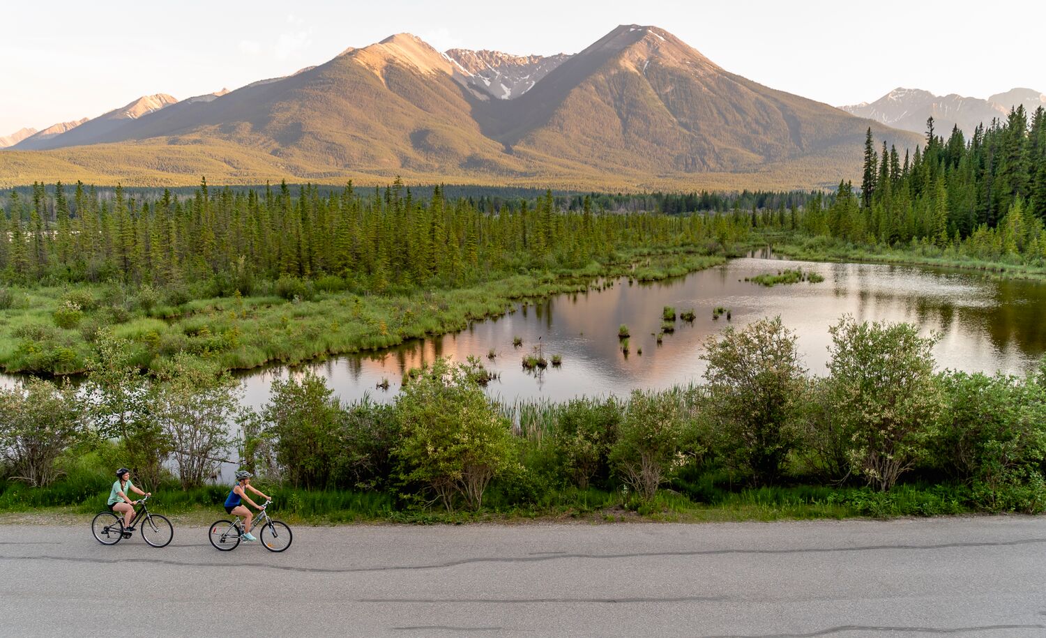 Two people bike along Vermilion Lakes Road at sunset in Banff National Park.