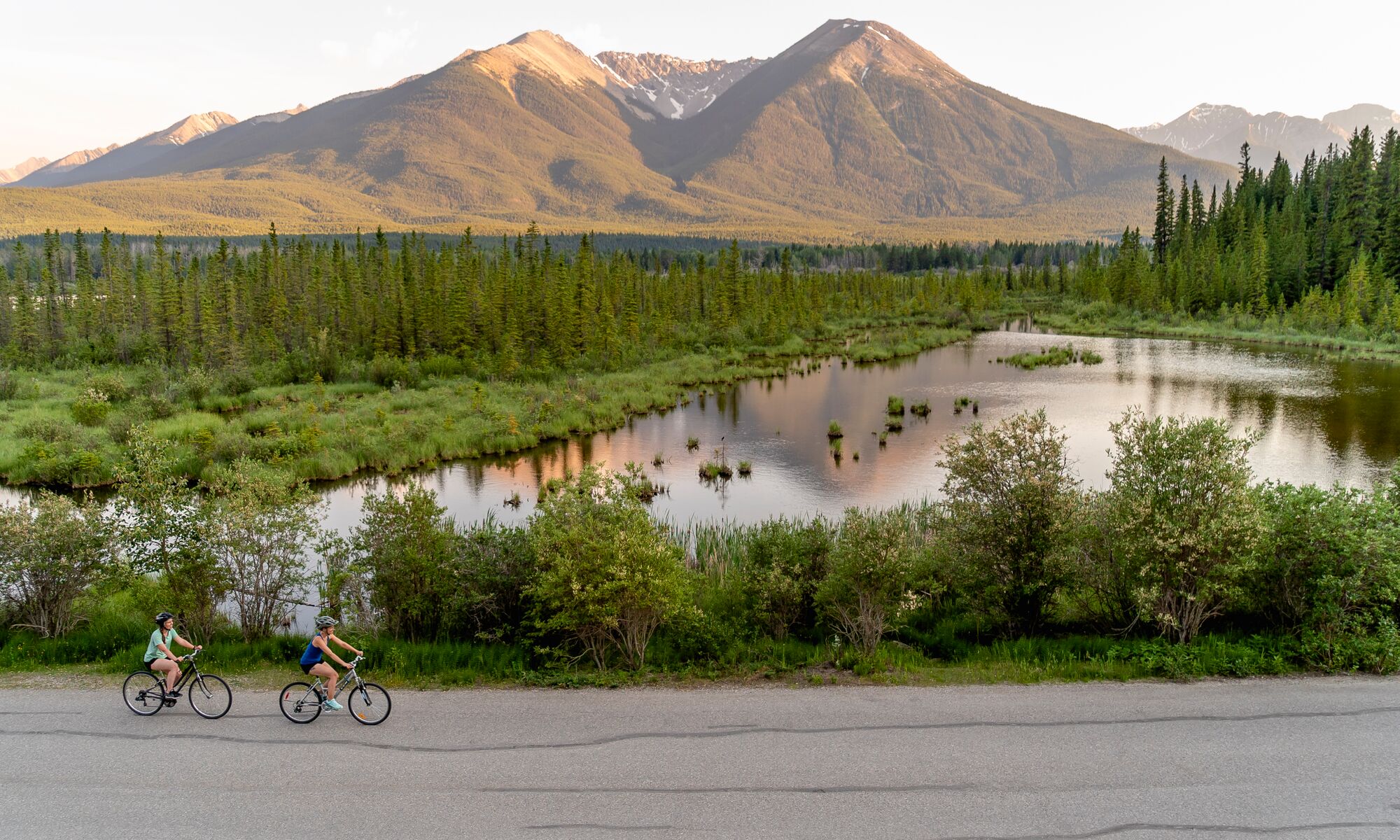 Two people bike along Vermilion Lakes Road at sunset in Banff National Park.
