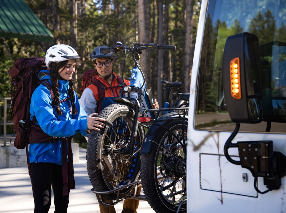 Two people mount bikes on the front of a Roam Transit bus to get to their mountain bike route in Banff National Park.