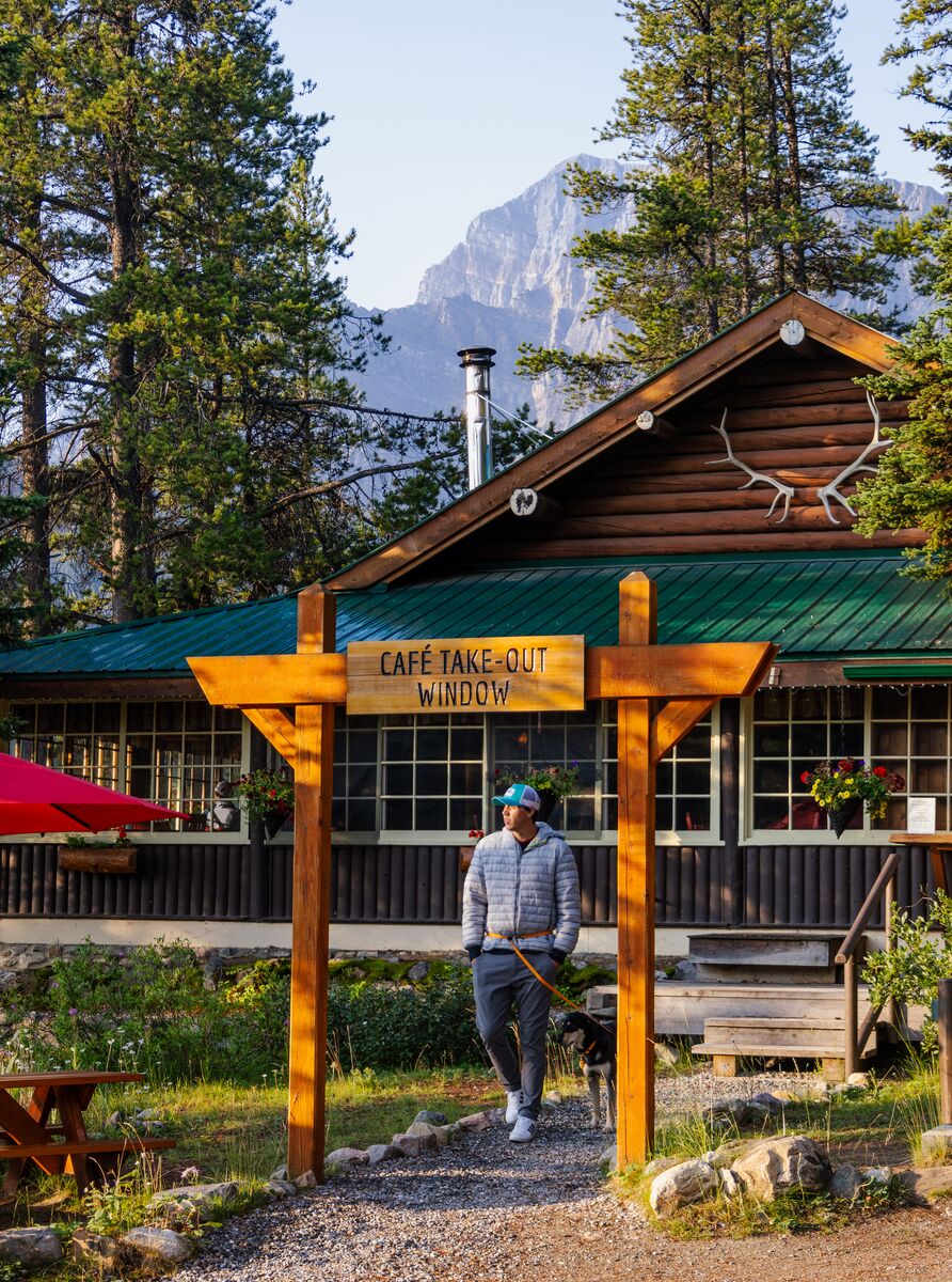 Rustic mountain lodge café surrounded by towering pine trees, with outdoor seating and scenic Rocky Mountain views.
