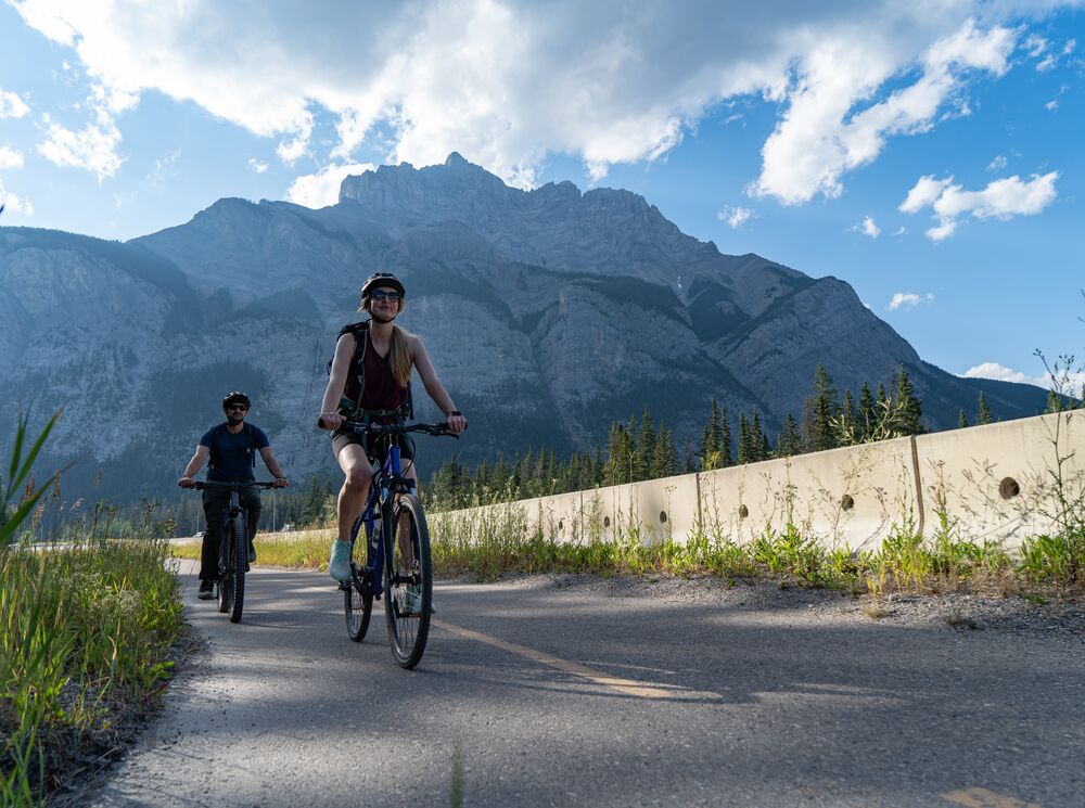 Two people bike along the Legacy Trail outside the Banff townsite on a bluebird evening in Banff National Park.