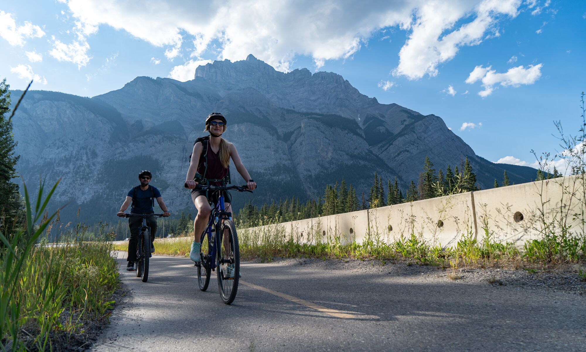 Two people bike along the Legacy Trail outside the Banff townsite on a bluebird evening in Banff National Park.