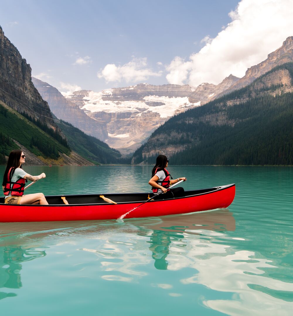 Two people canoeing on the turquoise waters of Lake Louise in a red canoe in Banff National Park.