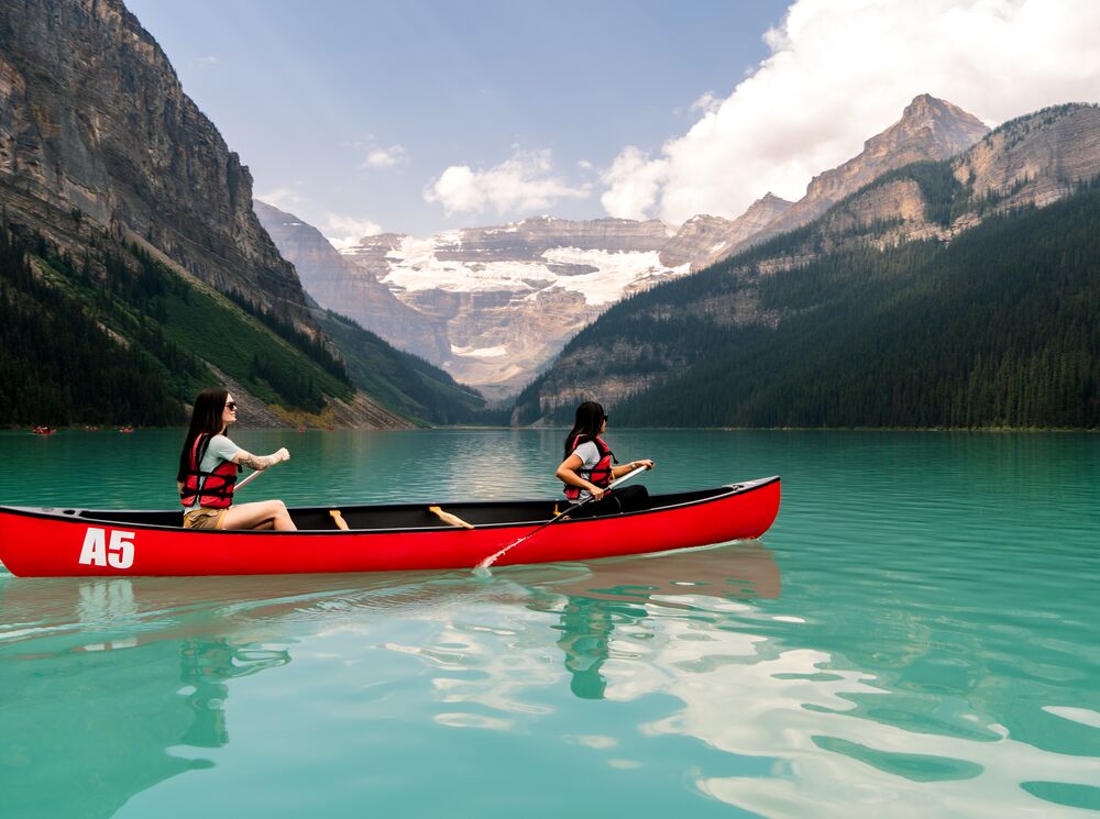 Two people canoeing on the turquoise waters of Lake Louise in a red canoe in Banff National Park.