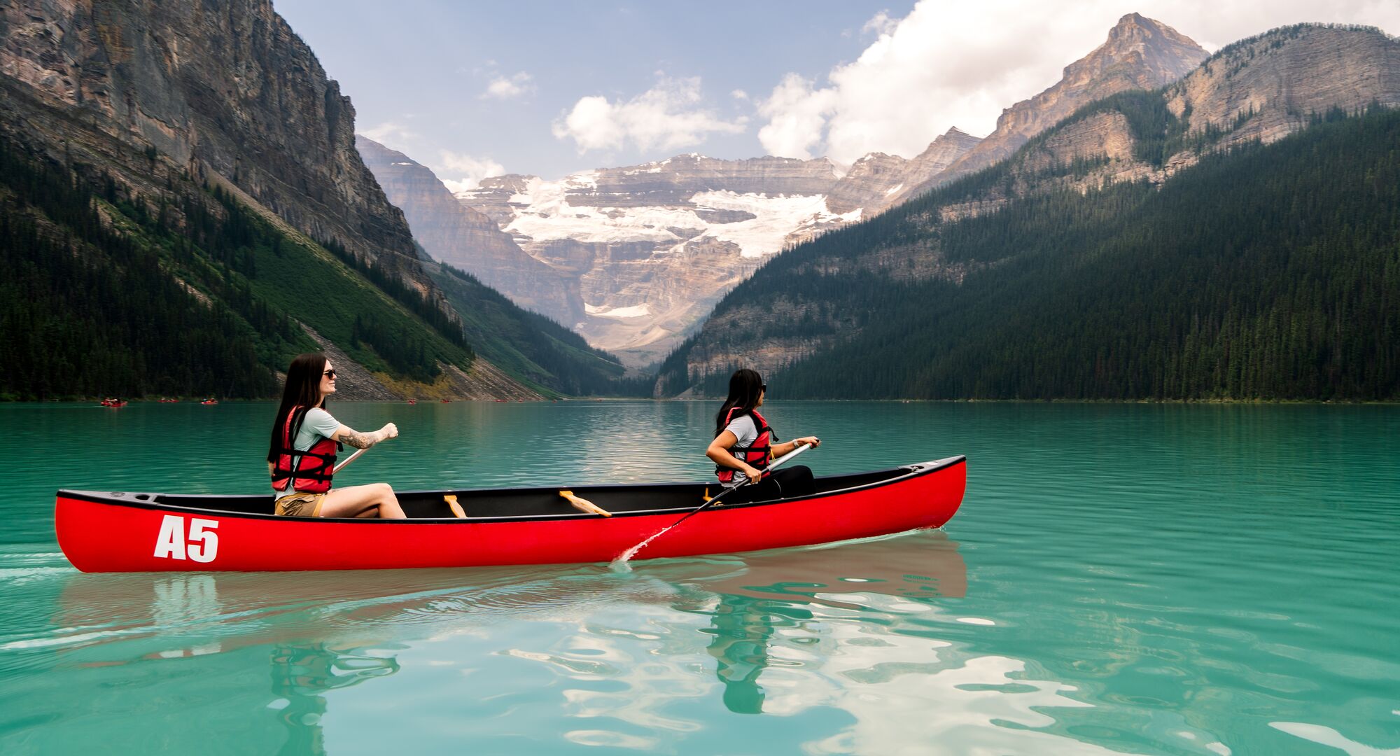 Two people canoeing on the turquoise waters of Lake Louise in a red canoe in Banff National Park.