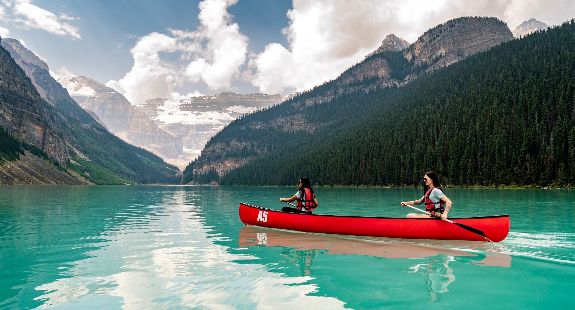 A view of turquoise Lake Louise from the shoreline on a summer day at sunset.