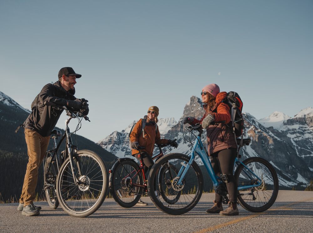 Three people stand with their electric bikes at the top of Moraine Lake Road in Banff National Park.