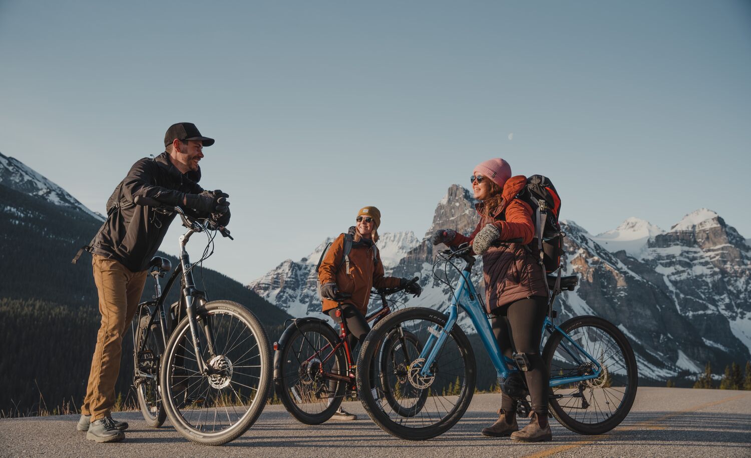 Three people stand with their electric bikes at the top of Moraine Lake Road in Banff National Park.