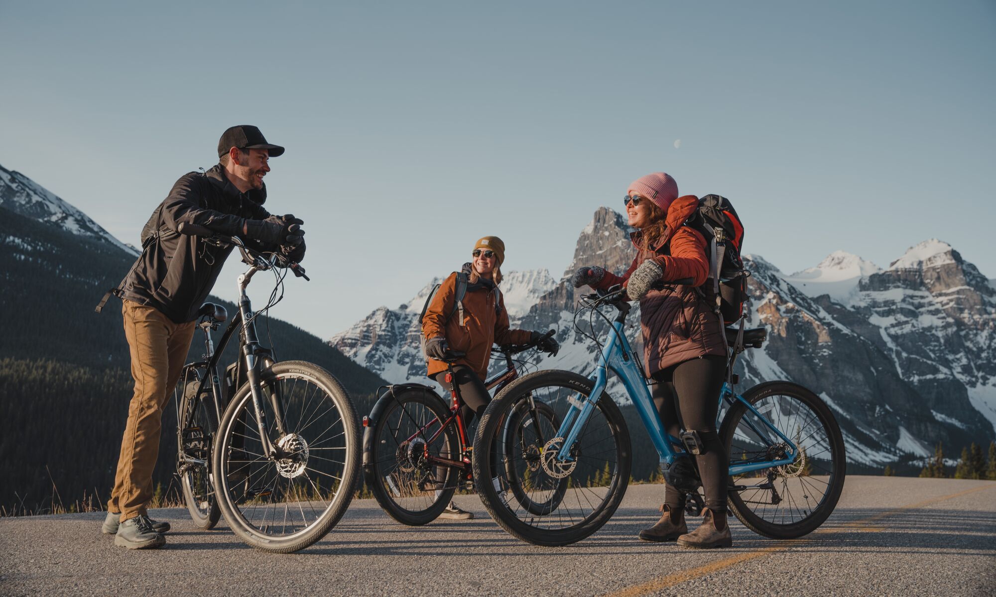Three people stand with their electric bikes at the top of Moraine Lake Road in Banff National Park.