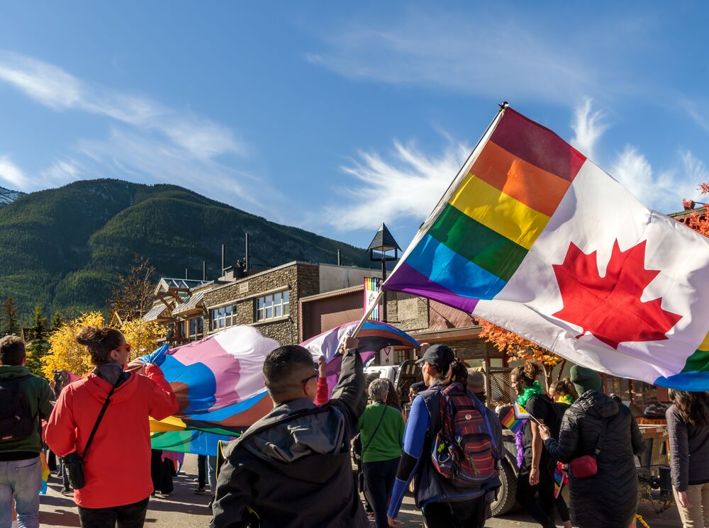 2SLGBTQIA+ community members, visitors, allies, and locals walk along Banff Avenue with a Canadian Pride flag during the Banff Pride Festival in Banff National Park, celebrating inclusion, diversity, and community at one of Canada's premier Pride events.
