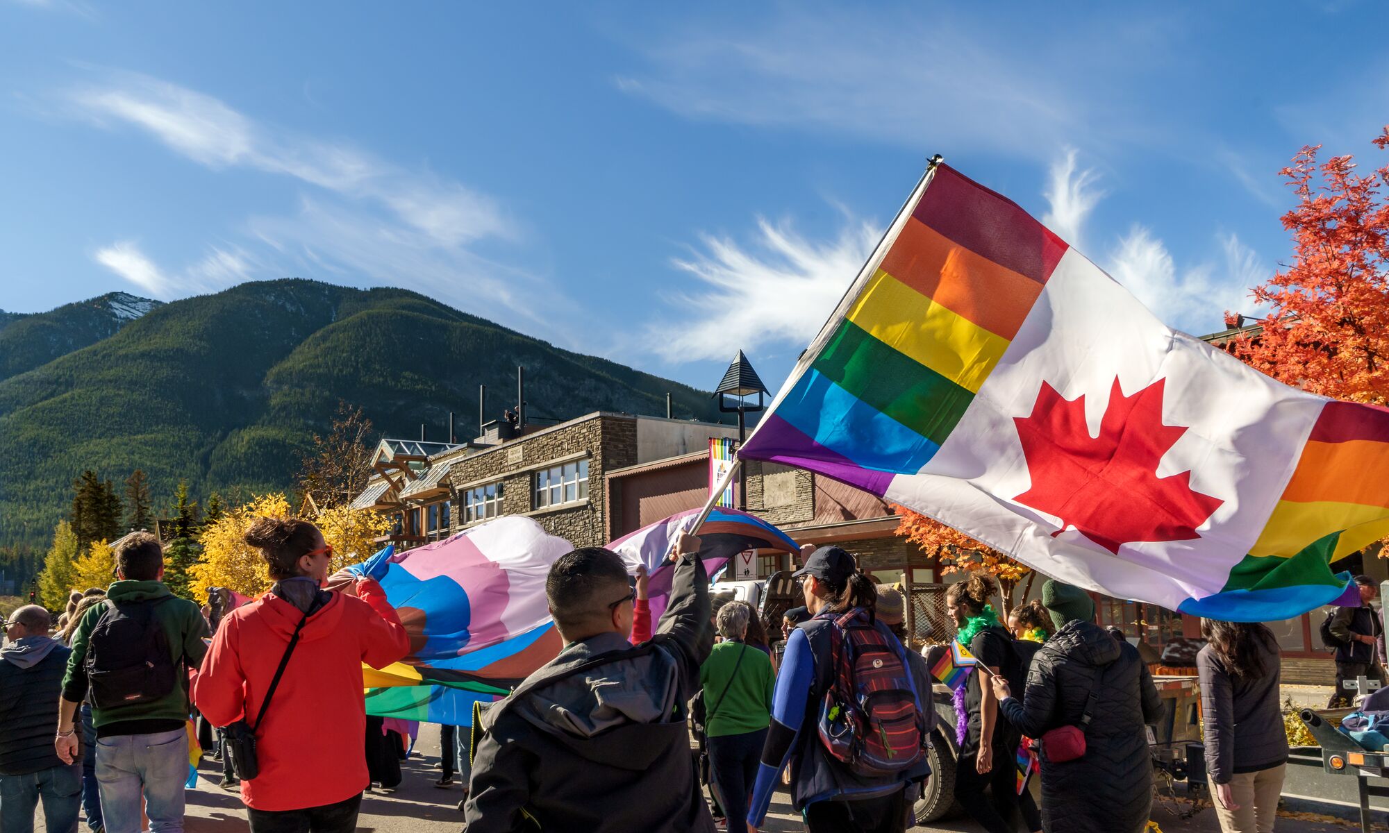 2SLGBTQIA+ community members, visitors, allies, and locals walk along Banff Avenue with a Canadian Pride flag during the Banff Pride Festival in Banff National Park, celebrating inclusion, diversity, and community at one of Canada's premier Pride events.