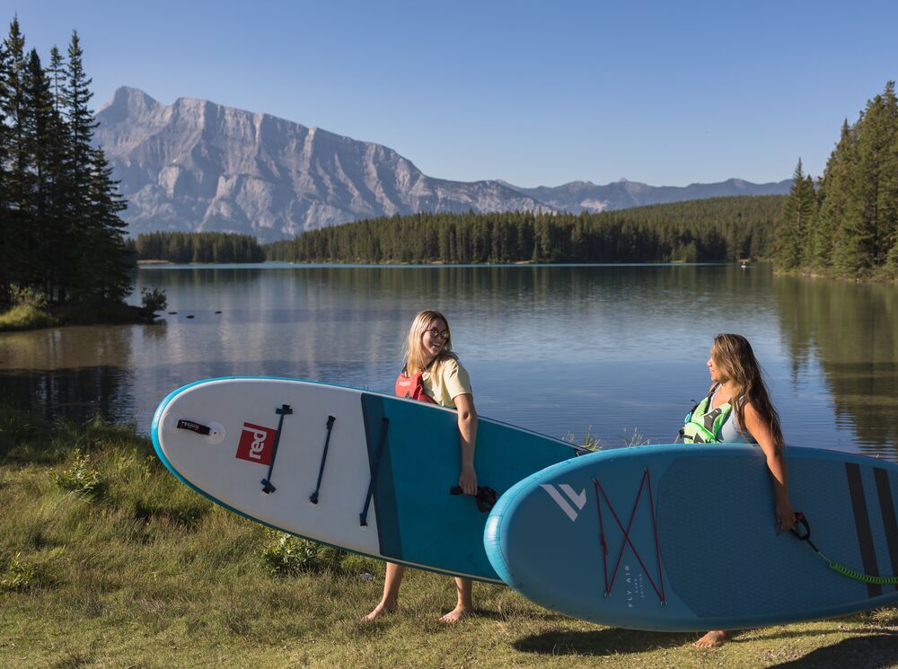 Two people carrying their paddle boards from Two Jack Lake in Banff National Park