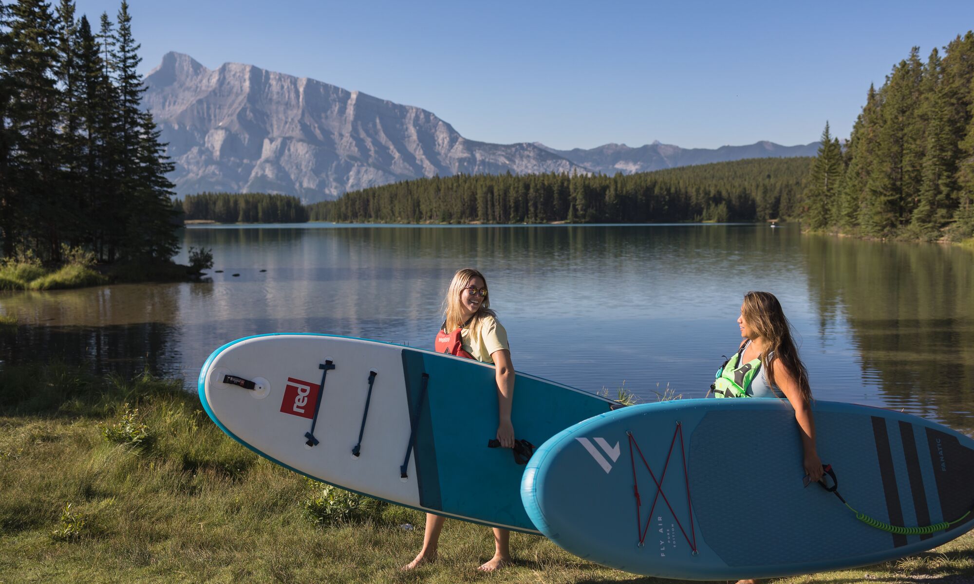 Two people carrying their paddle boards from Two Jack Lake in Banff National Park