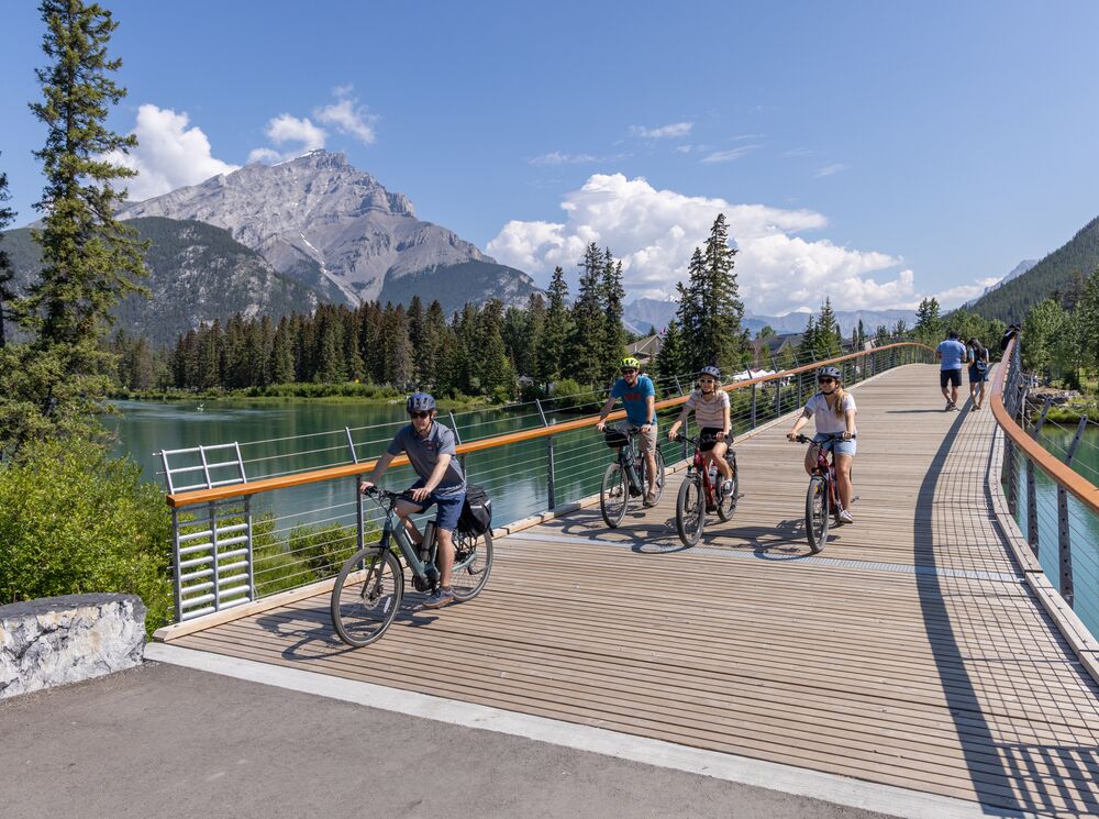 Four people biking over the Banff pedestrian bridge in Banff National Park