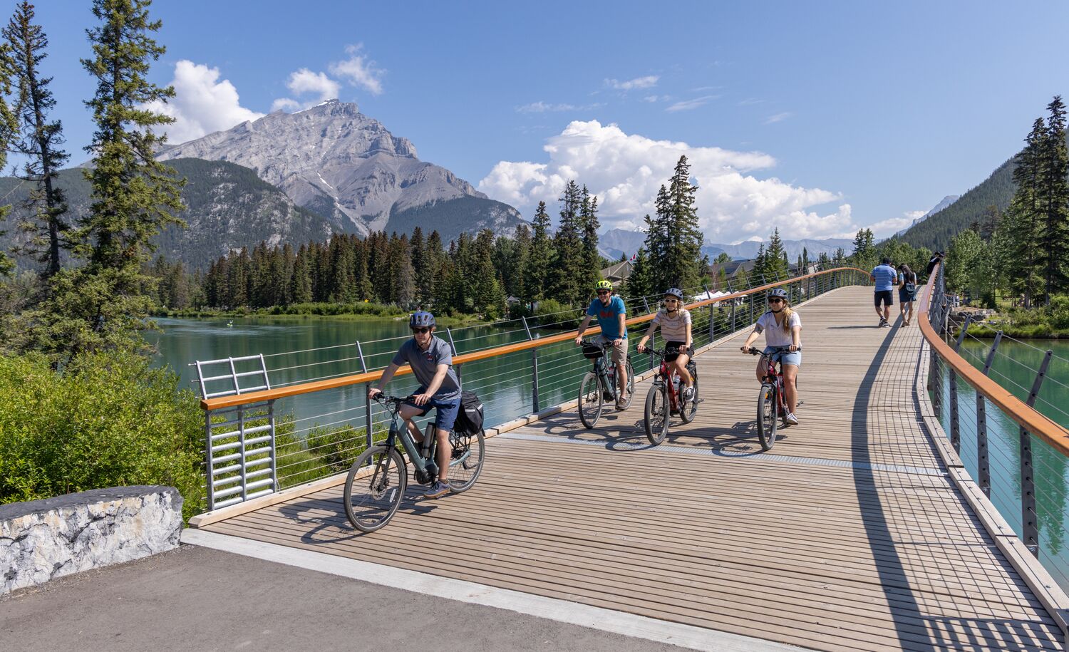 Four people biking over the Banff pedestrian bridge in Banff National Park