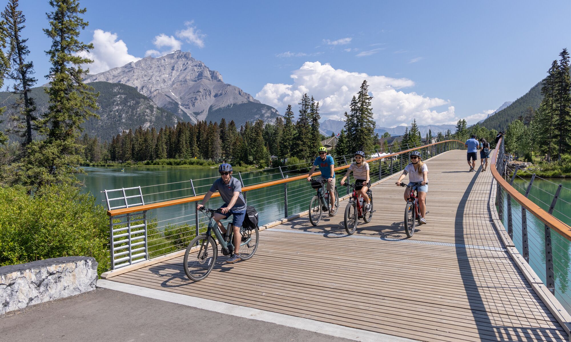Four people biking over the Banff pedestrian bridge in Banff National Park