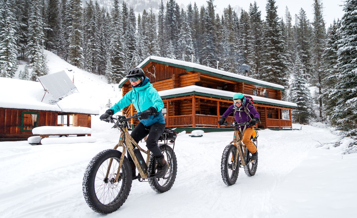 Two cyclists ride e-fat bikes away from Sundance Lodge in the winter while biking in Banff National Park.