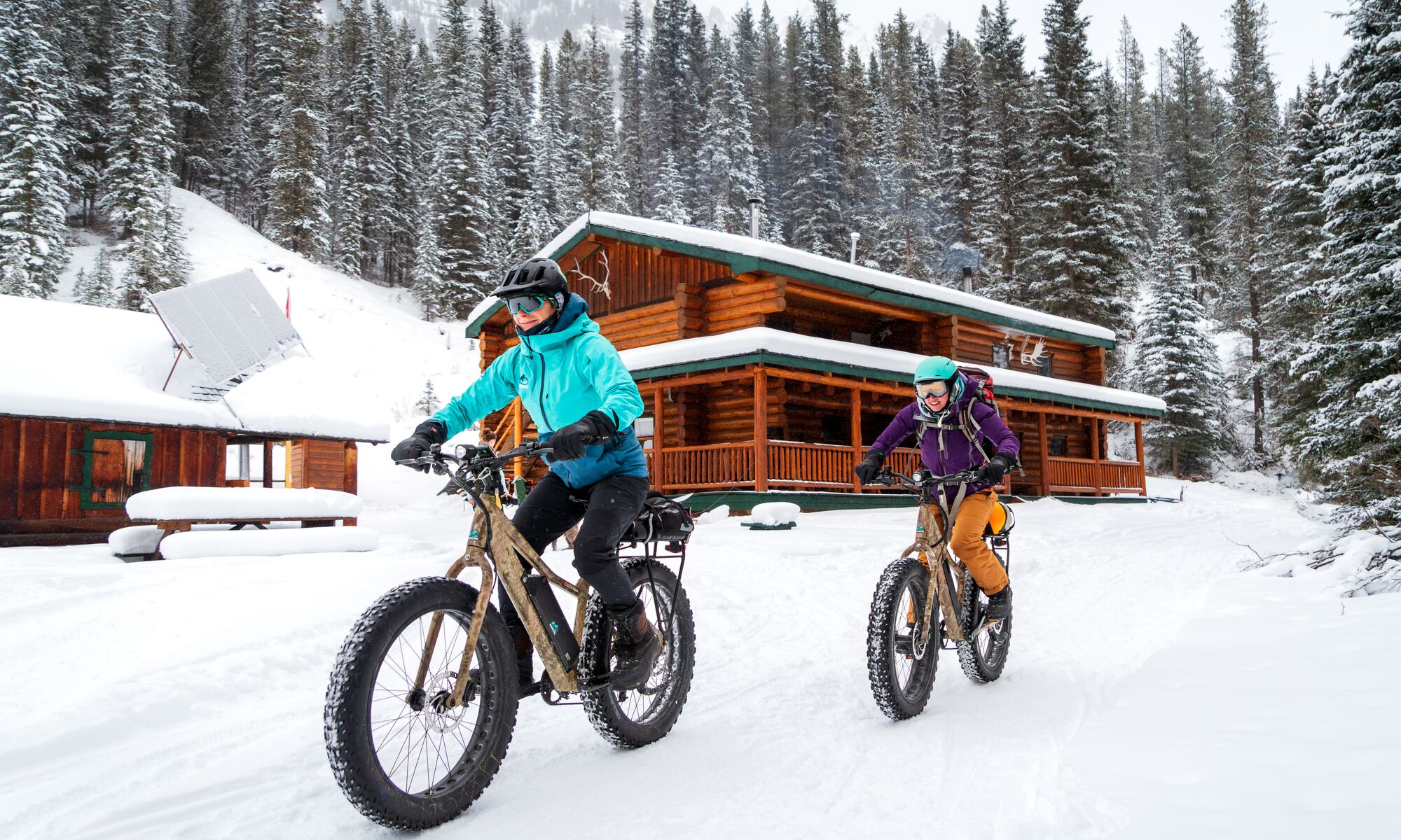 Two cyclists ride e-fat bikes away from Sundance Lodge in the winter while biking in Banff National Park.