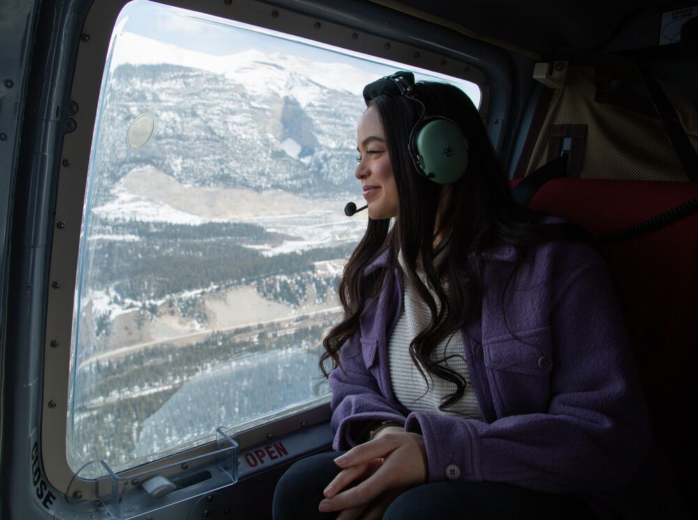 A female sitting in a helicopter flying over the Canadian Rocky Mountains