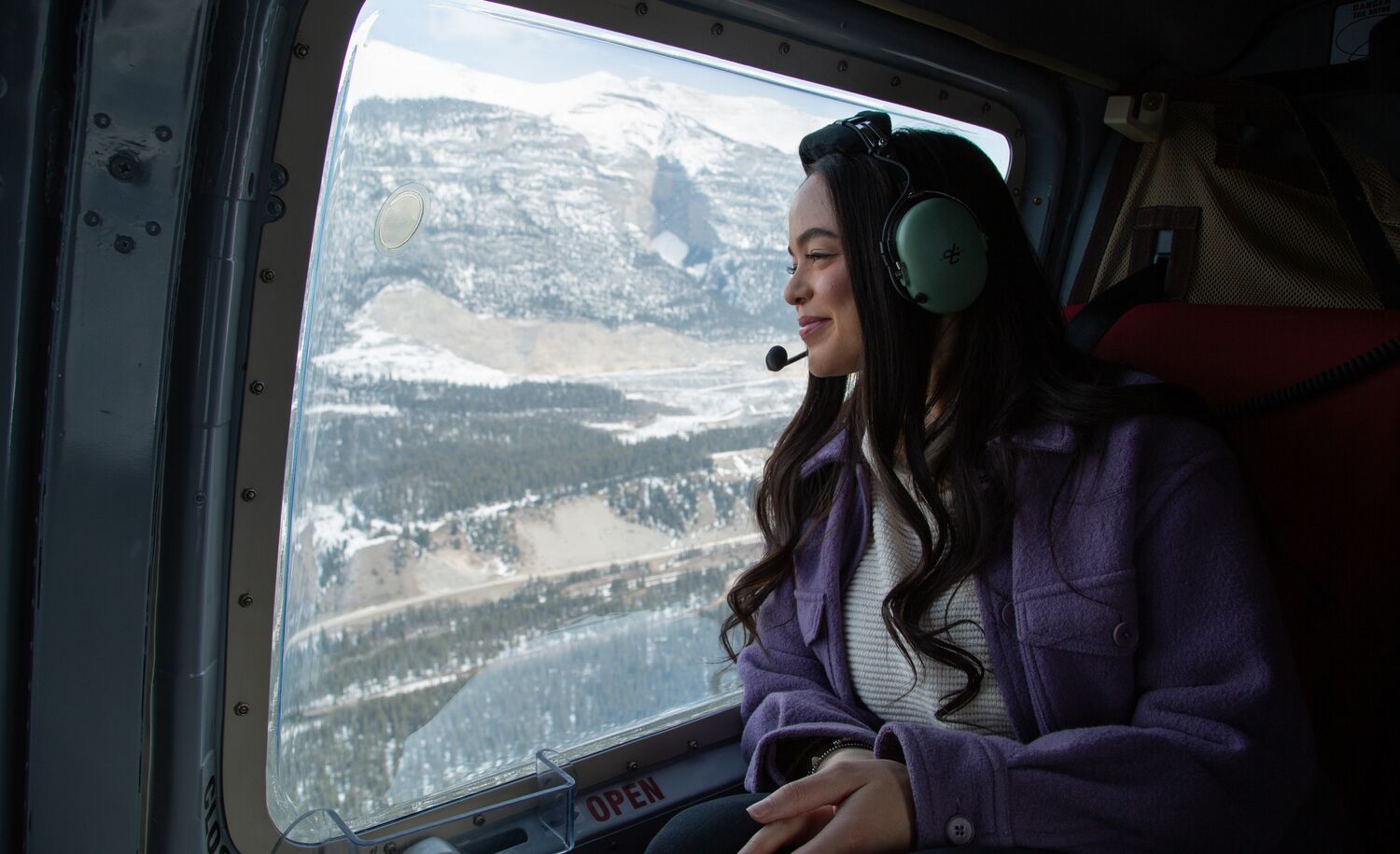 A female sitting in a helicopter flying over the Canadian Rocky Mountains