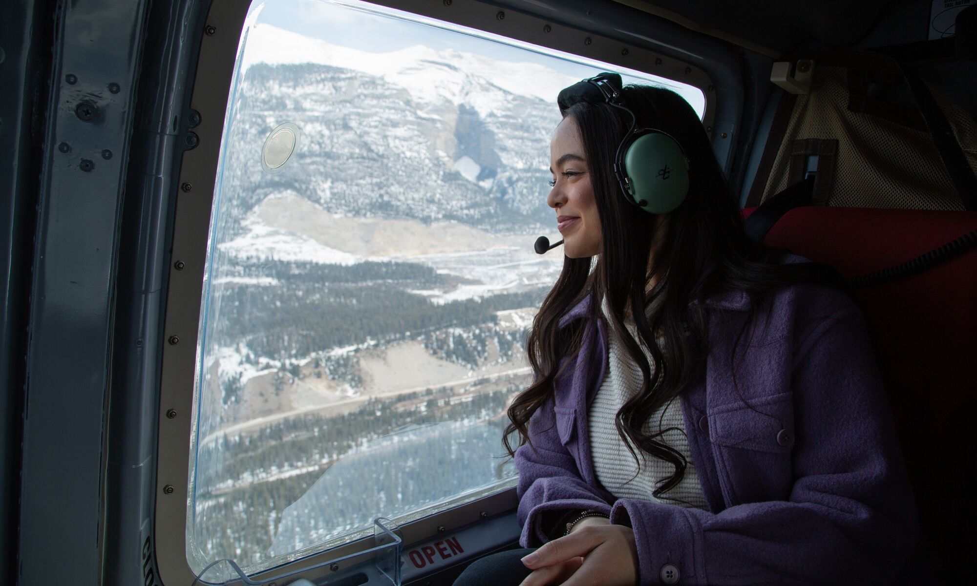 A female sitting in a helicopter flying over the Canadian Rocky Mountains