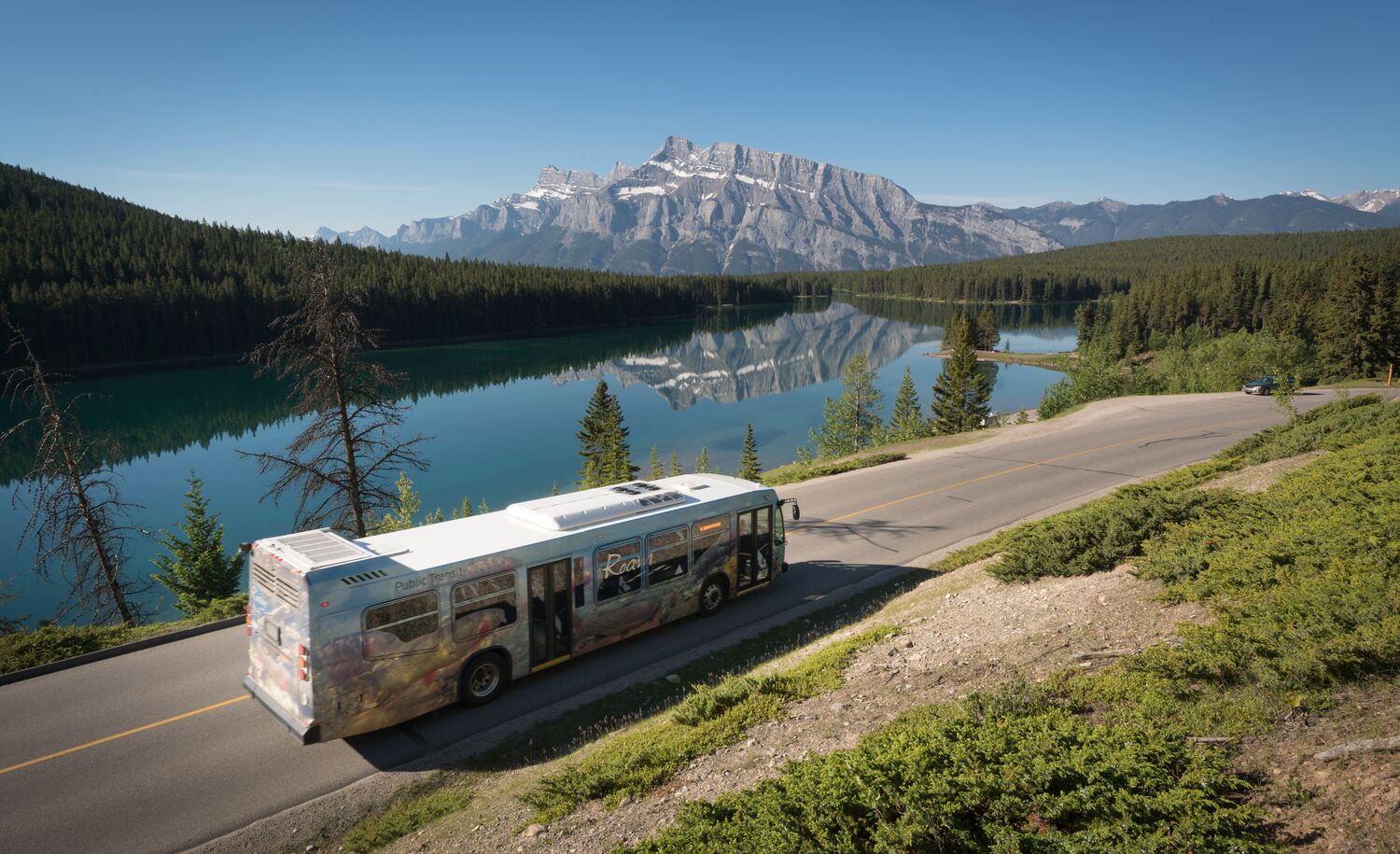 A Roam Transit bus driving past Two Jack Lake in Banff National Park