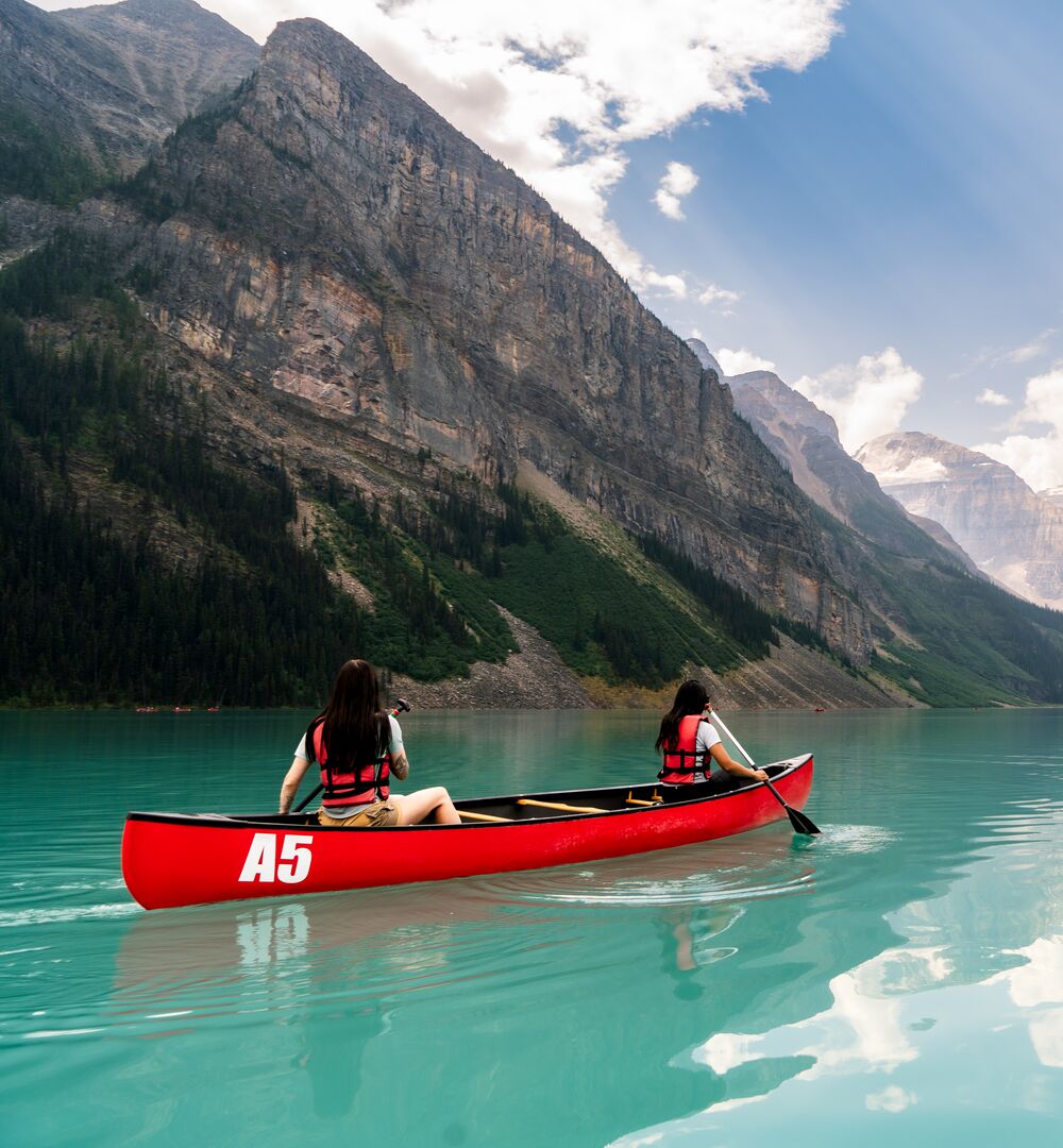 Two people paddling a red canoe on a summer day on Lake Louise in Banff National Park.