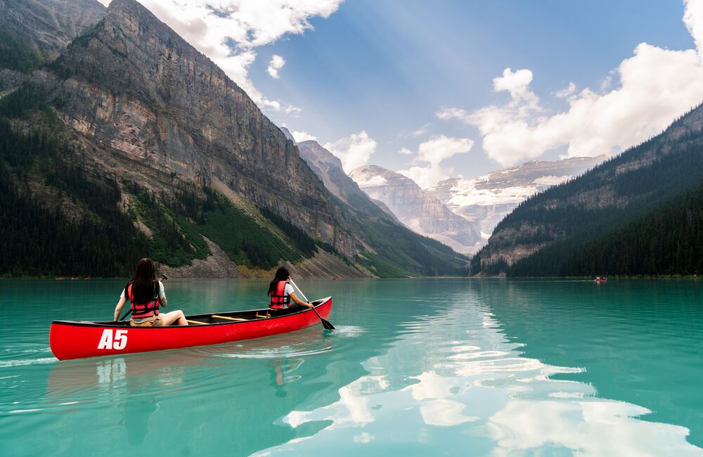 Two people paddling a red canoe on a summer day on Lake Louise in Banff National Park.