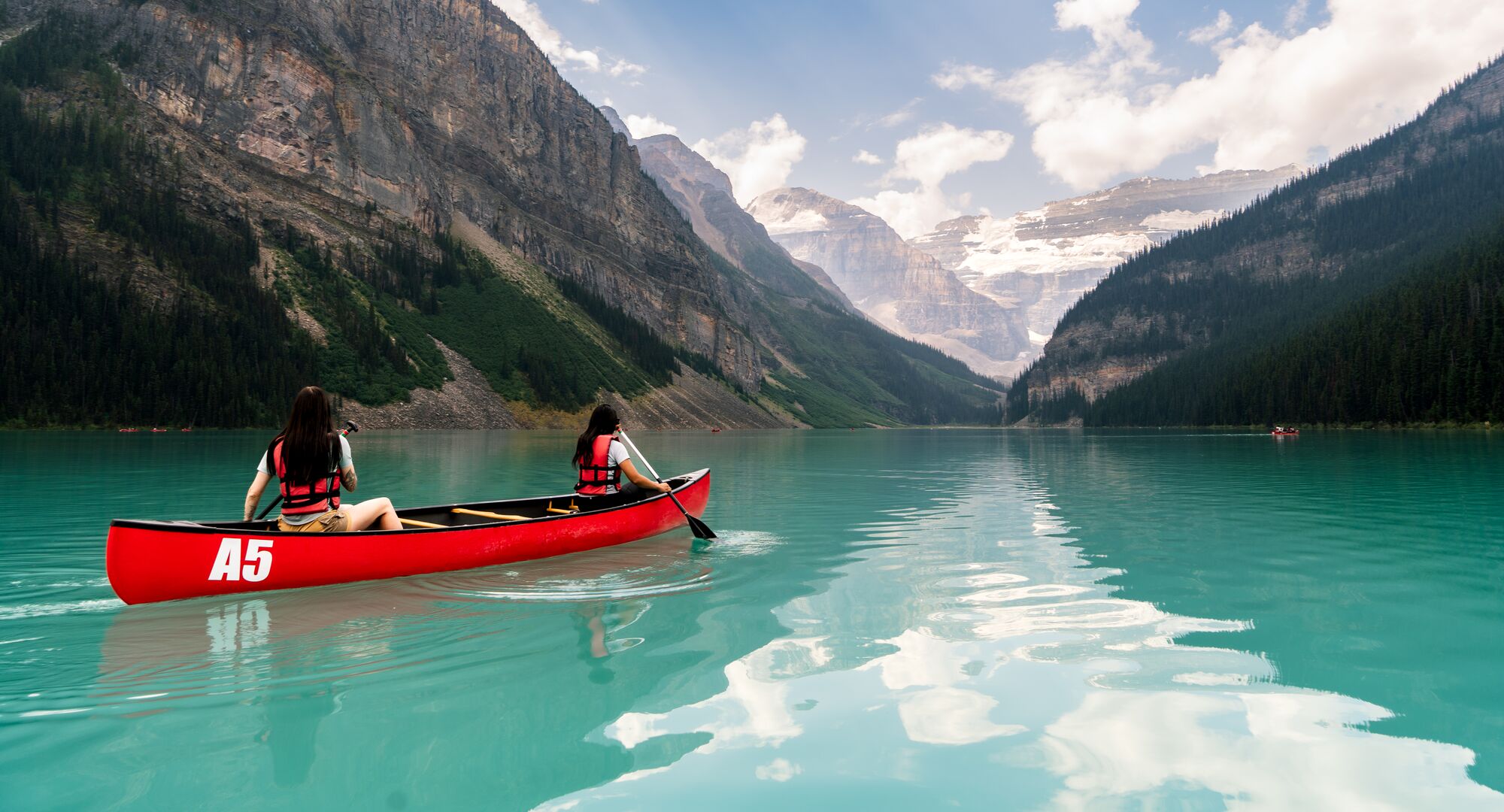 Two people paddling a red canoe on a summer day on Lake Louise in Banff National Park.