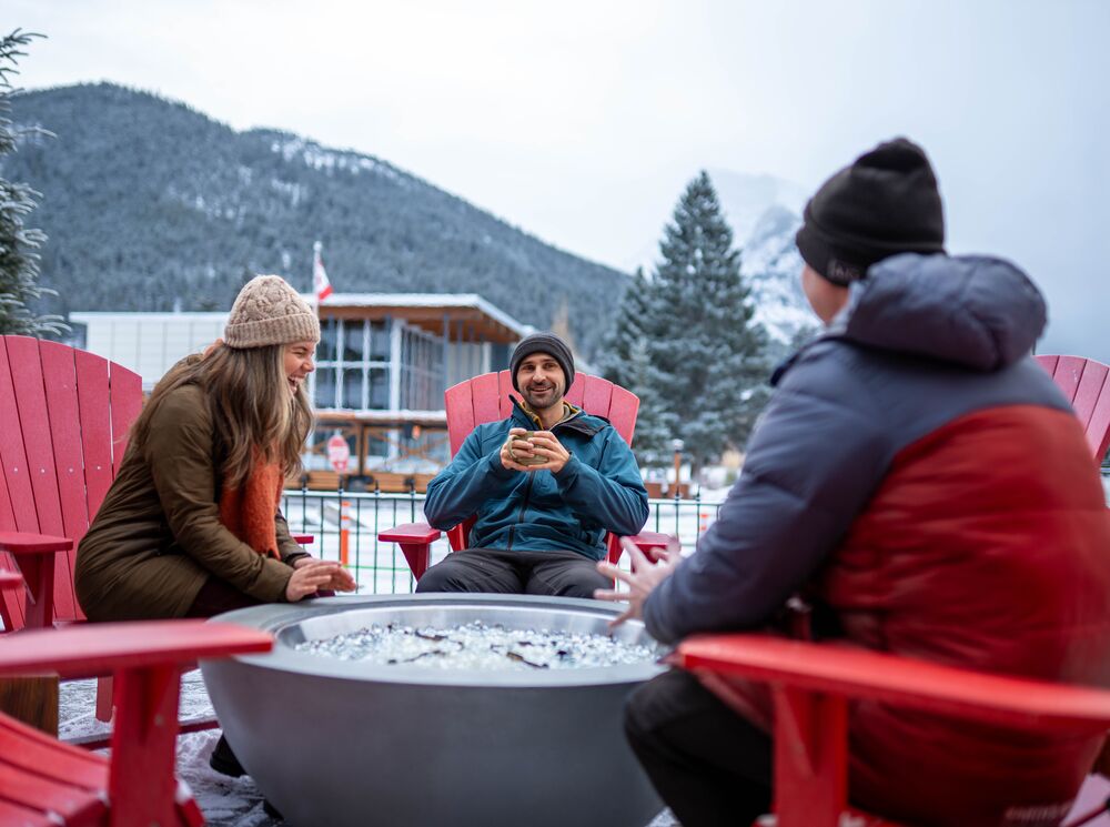 Three people sitting by a fire outside in Winter in Banff National Park
