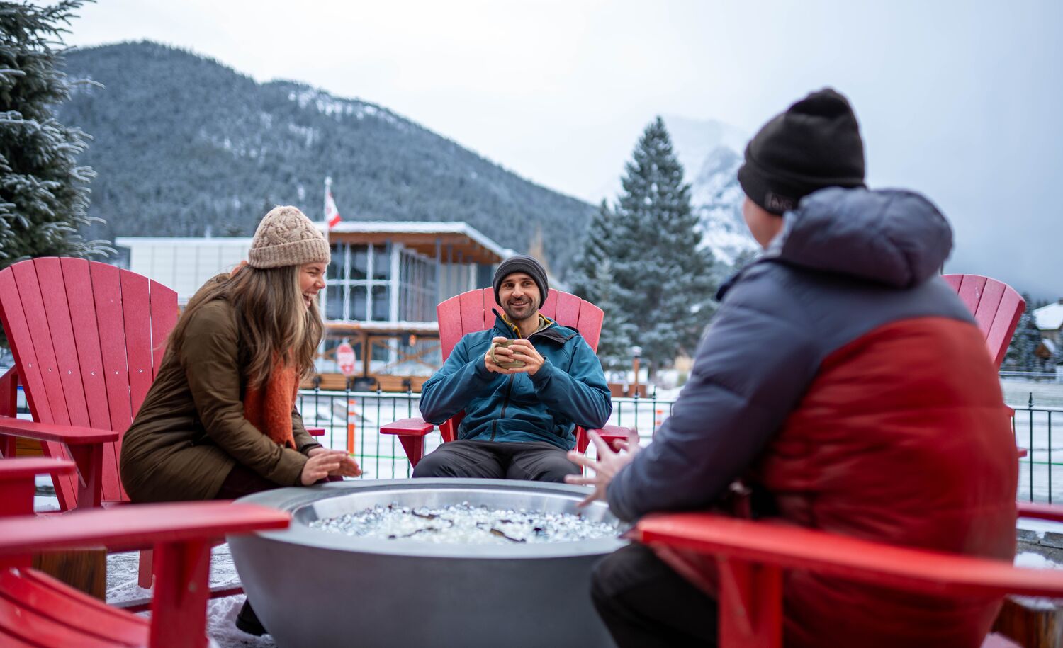 Three people sitting by a fire outside in Winter in Banff National Park
