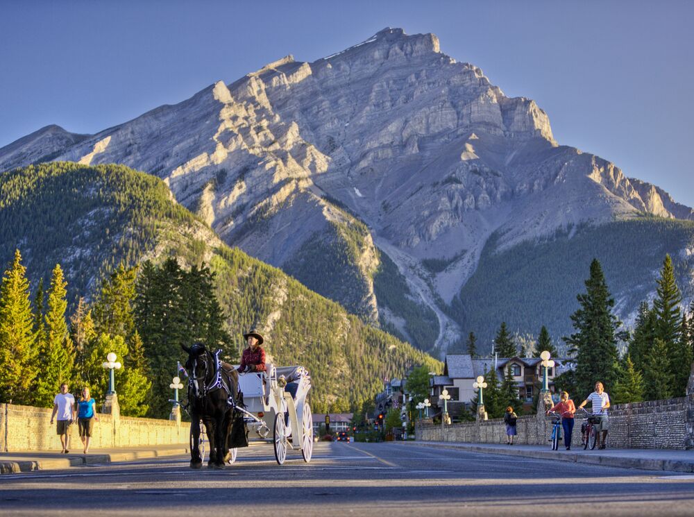 A horse-drawn carriage going down Banff Ave with Cascade Mountain in the back in Banff National Park