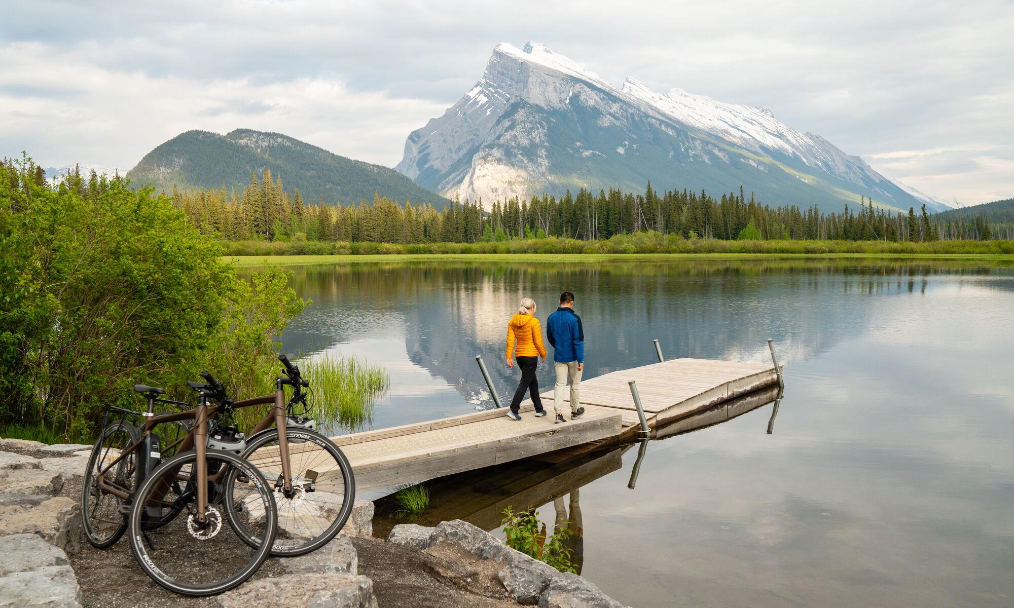 Two people stand at the end of a dock at Vermilion Lakes in Banff after